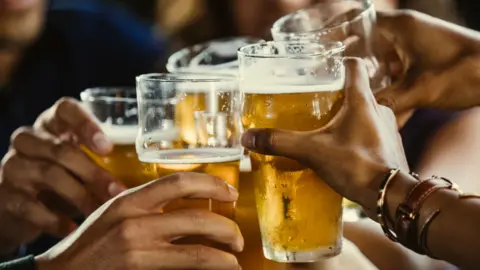 AFP via Getty Images A close up image of five people toasting with pint glasses of lager.