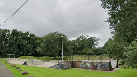 Skatepark in Okehampton. Graffiti is on the side of the skatepark. Grass is surrounding the site. 