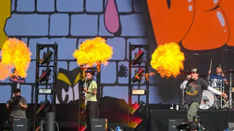 A band on stage with balls of flames burning behind them