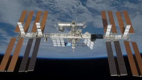 The International Space Station is seen in the centre of the image in space orbiting the Earth