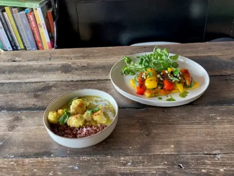 The cafe's dhal and polenta pizza dishes. They are served on white crockery on a wooden table with a bookshelf in the background.