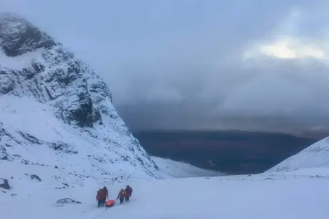 Lochaber MRT Members of Lochaber MRT haul a stretcher over snow in a snowy mountain landscape.