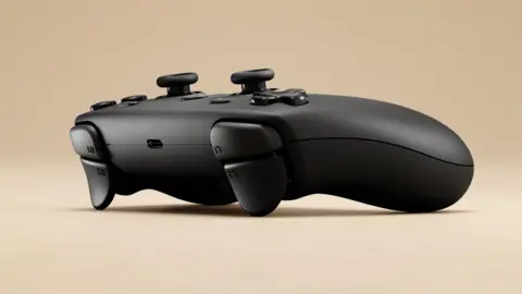 Valve A promotional image of the Steam Controller, seen from the front and side. It is a charcoal black gamepad, laid on a beige surface and background.