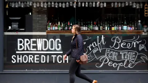 Getty Images A woman walks past a Brewdog bar in London. On the glass is written Brewdog Shoreditch and Craft Beer for the People.