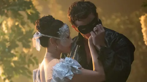 Netflix Sophie (Yerin Ha), wearing a silver mask and silver dress, and Benedict (Luke Thompson), wearing a black mask and black bolero jacket.