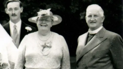 The family of Eileen Elgar A black and white image of Eileen Elgar with Alfred, her husband, and another man behind them. She is wearing a hat.