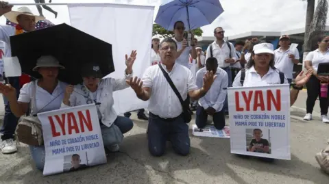 EPA People dressed in white are kneeling down, holding up signs demanding the release of a kidnapped boy in Jamundí