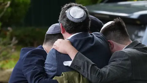 Three men wearing Jewish skullcaps - known as a kippahs - embrace in grief on the street after the attack