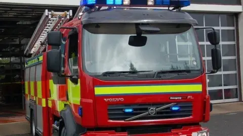 A red fire engine with its blue lights on driving out of a fire station. 