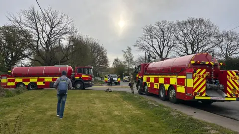 Two fire engine water tankers parked on a road with a grassy verge in the foreground.