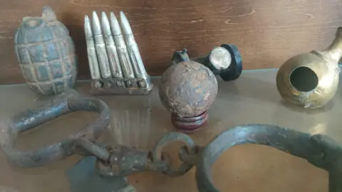 Gareth Morris A grenade, a rack of bullets, cannon ball and a pair of Victorian handcuffs in a display cabinet. 