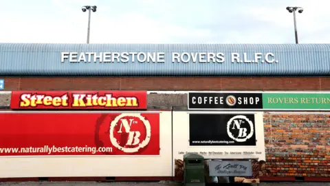 Getty Images The outside of Featherstone Rovers R.L.F.C's ground, as indicated by letters emblazoned across a corrugated steel front. Food and drinks stalls, which appear to be shut, sit in front of it.