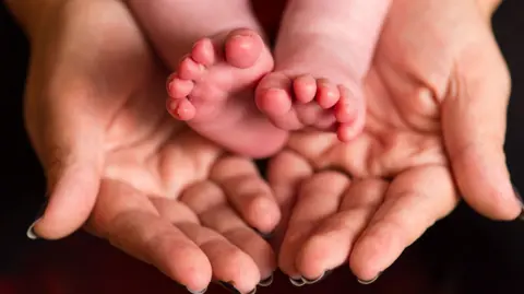 A baby's tiny feet outstretched in the cupped hands of a woman.