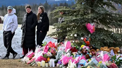 Reuters A group of four people walk past a makeshift memorial made up of flowers, candles and teddy bears near a pine tree in the town of Tumbler Ridge