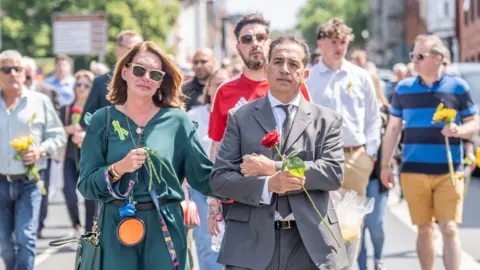 Danny Lawson/PA Wire Two people walking together holding hands, the woman wears a green dress and the man wears a grey suit. 