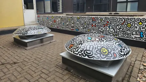 East Sussex Healthcare NHS Trust Doodle mural on a low wall and round stone objects in an outdoor stone courtyard