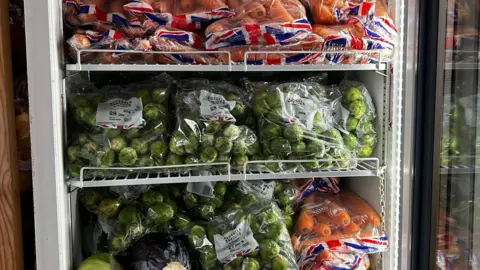 Shepton Mallet Community Fridge Three shelves of a large upright fridge full of bags of carrots and Brussels sprouts