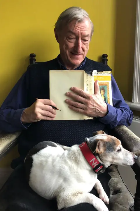 Julian Barnes Julian in dark blue shirt, seated, with a book on his hand, looking fondly at his Jack Russell, Jimmy