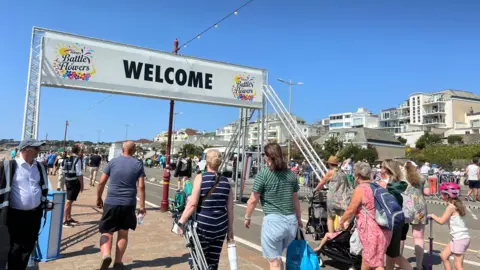 People walking under a 'Welcome' sign. 