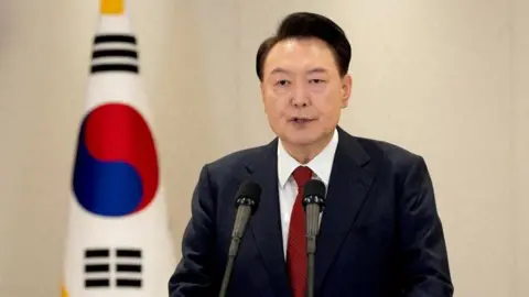 Yoon in a suit in front of a South Korean flag talking into a mic