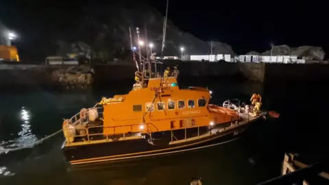 RNLI lifeboat, yellow in colour in night time, surrounded by water. 