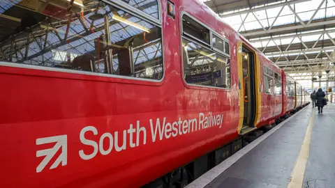 A red South Western Railway train on a platform. It has its door open.
