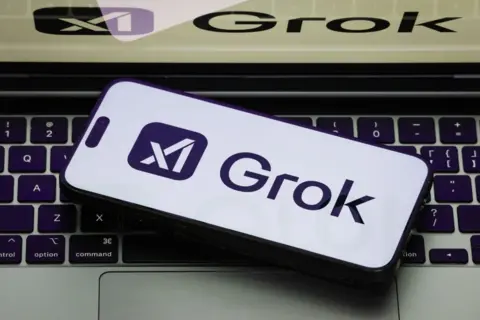 Getty A picture of the Grok logo on a white background phone, which is resting on an open laptop which is also showing the Grok logo.