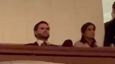 JD Vance and Usha Vance sit behind a white half wall.