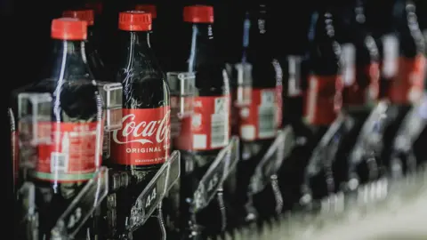 Bottles of Coca Cola pictured in a beverage dispenser.