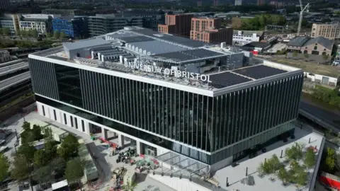 Artist's impression of a new building which says University of Bristol on the top. The building has a glass front and a forecourt with trees.