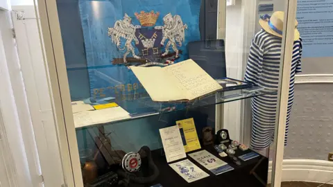 A glass cabinet with artifacts and a mannequin with a blue-white striped swim suit