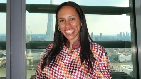Supplied Harriet Hemmings wearing orange, red and white jockey silks in front of the London skyline.