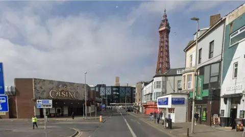 Google streetview of Central Drive with Coral Island casino on left and shops on the right. Blackpool Tower rises above against a clouded blue sky