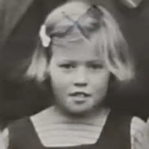 Fiona Brown A black and white photograph of a child Moira with short fair hair, and a bow clip on the left. 