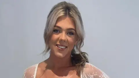 Family handout Amy Doherty who has light blonde hair partly pulled back over her left shoulder, she is wearing a white lace top and smiling at the camera.