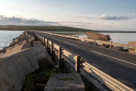 Getty Images A road across a causeway, with water on either side and shipwrecked boat on the right hand side of the road.