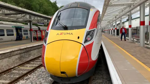 BBC/Tom Ingall Front view of a red and yellow LNER Azuma train alongside a station platform.