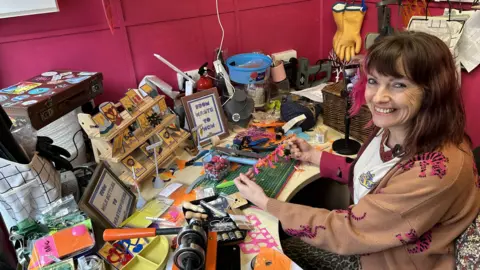 Louise Lee sat in her packed workshop surrounded by materials and proudly showing a pink and orange necklace made from inflatables.