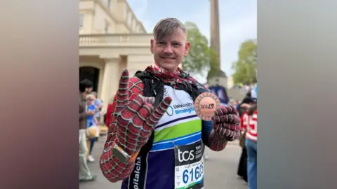 A man dressed as Spider-Man holds a medal in front of a statue.