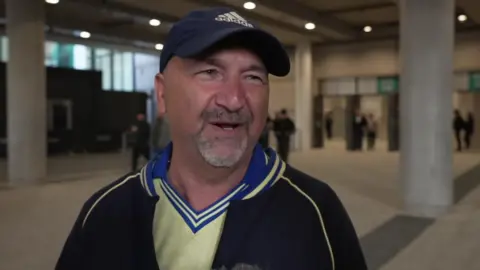 A man in a cap talking to a reporter after the Saints game at Wembley.