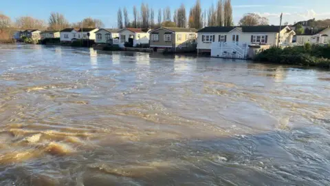 The River Stour at a very high level with a row of mobile homes at the far side of the river.