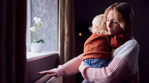 Getty Images A mother with her child trying to warm up in front of a radiator at home - Stock photo