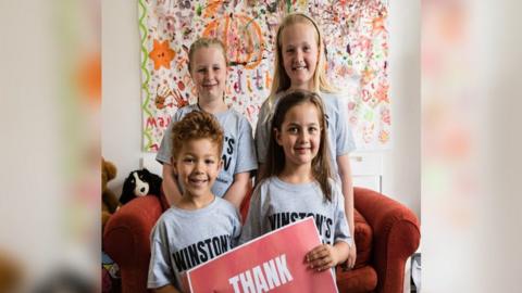 Four children wearing Winston's Wish T-shirts, holding a sign that say "Thank you"