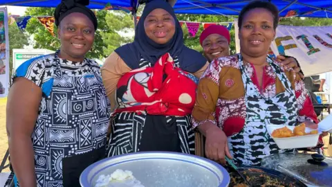 From left to right Ltoya Augustt, Fati Tourau,Sadiya Abdullahi and Ivon Kayitesi of the African food stall smiling for the camera and putting food in containers.