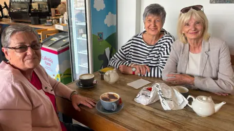 Three women sat around a table drinking teas and coffees.