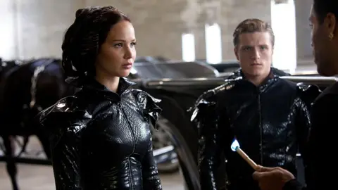 Mockingjay Part 2 shows Jennifer Lawrence and Josh Hutcherson in costume, being addressed by a third character just off-screen.