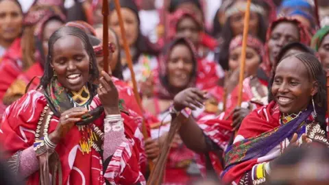 Borana women carry carved wooden sticks and march in matching red clothes.