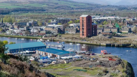 Getty Images An image of Dumbarton's waterfront, pictured from the top of Dumbarton Rock, including various industrial buildings as well as yachts along the waterfront