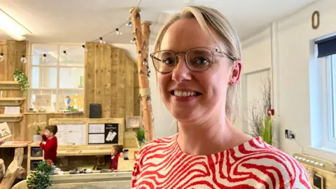 Teacher Sam Barker in woodland-themed classroom smiling at camera