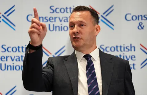 PA Media Russell Findlay pointing towards journalists at the media conference for his election as leader. He is standing in front of Scottish Conservative party branding.